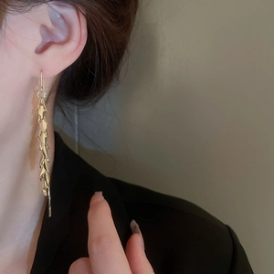 Close-up of golden leaf tassel earrings with metallic chain texture on a model