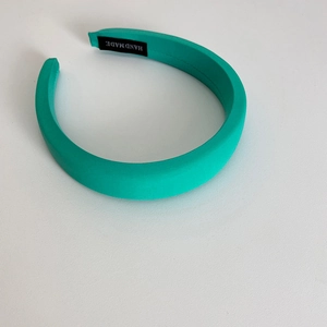 Detail view of a teal green padded headband with an authentic HAND MADE interior label
