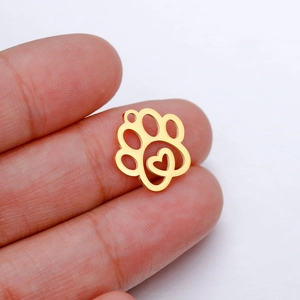 Macro shot of small golden paw pendant with heart cutout held on a fingertip
