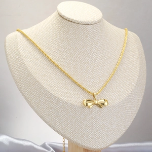 Elegant gold bow necklace on display stand with minimalist silk fabric decoration
