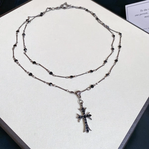 Detailed view of Gothic cross necklace with black gemstones on a textured board
