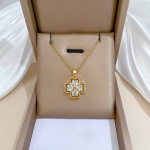 Gold clover necklace with heart shaped crystals displayed in a beige velvet jewelry box