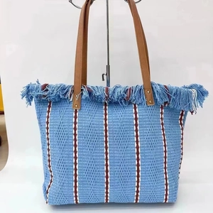 Blue woven beach tote bag with fringe details and stripes on a display stand