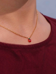 Dettaglio di una collana dorata con pendente a mela rossa indossata da una modella