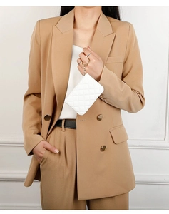 Close-up of a white quilted mini pouch with gold hardware held by a woman in a suit