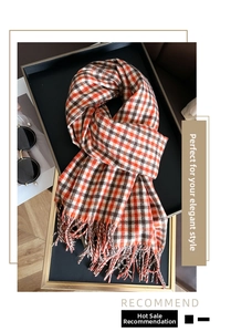 Detail of orange and brown plaid scarf with fringe tassels on a decorative tray
