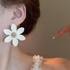 Close-up of sweet white floral tassel earrings worn by a model with a soft warm lighting
