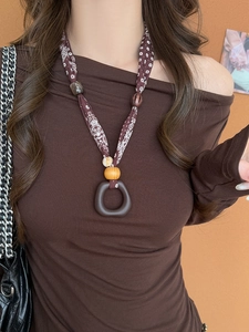 Detail of ethnic style necklace featuring brown fabric strap and geometric round pendant