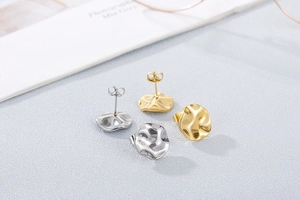Detailed macro view of irregular wavy hammered round metal stud earrings in gold and silver