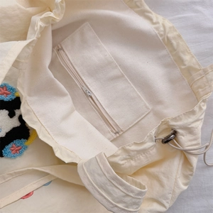 Detail of cream canvas tote bag showing inner zipper pocket and drawstring closure