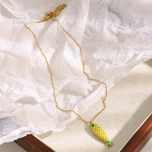 Detail of 18K gold plated necklace featuring a yellow enamel fish pendant on white texture