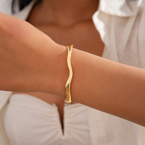 Detail shot of a minimalist 18k gold plated wave bangle on a female wrist