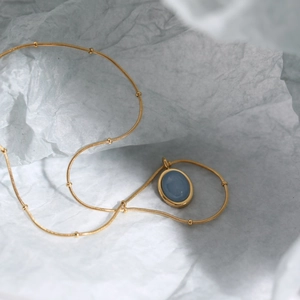 Detailed view of the 18K gold plated necklace with blue oval stone on textured paper