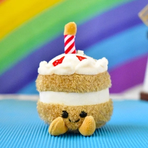 Close-up of a cute plush cake toy with a smiley face and a red striped candle decoration.