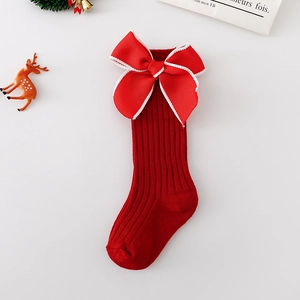 Detail of red Christmas socks for babies featuring a large velvet bow and ribbed texture