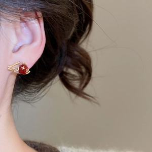 Detail showing 18k gold plated star and red apple stud earrings on model's ear