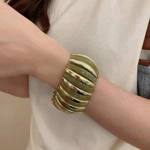 Detail of multi-layer gold metal and green resin beaded bracelet on a model's wrist