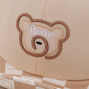 Close-up of baby beige cotton cap with bear embroidery and plaid brim detail