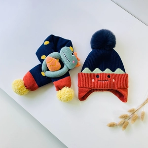 Detail of knitted baby hat and scarf set with cute monster face and dinosaur toy