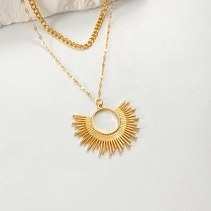 Détail du collier doré à deux rangs avec pendentif soleil rayonnant sur pierre blanche