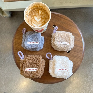 Close-up of four plush earbud pouches in grey, beige, brown and white on a wooden stool