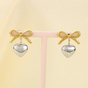 Detailed macro view of gold ribbon bow and silver heart pendant earrings on a pink stand