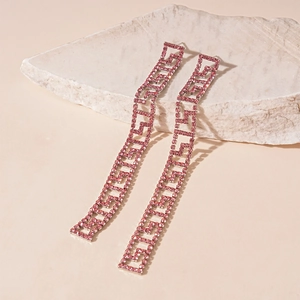 Macro shot of pink rhinestone geometric long earrings on a textured stone prop