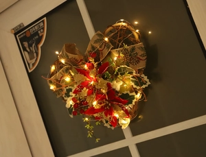 Close-up of heart Christmas wreath with poinsettias, burlap bow and warm LED lights