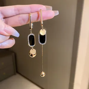 Close-up of asymmetric gold drop earrings with black geometric plates and pavé crystals