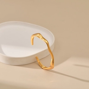 Detalle de un brazalete dorado con diseño ondulado sobre una bandeja de cerámica blanca