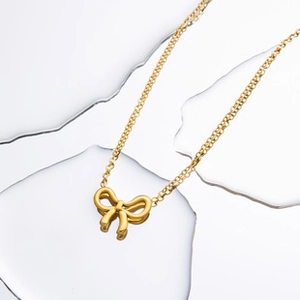 Detailed view of an 18K gold plated bow pendant necklace on a liquid metal background