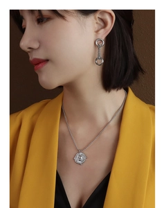 Detail view of a silver irregular coin pendant necklace on a model in a yellow suit
