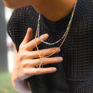 Detail of layered gold necklace with palm tree pendant and colorful beaded strand