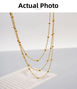 Detail of a triple-layered gold satellite chain necklace with smooth beads in titanium steel