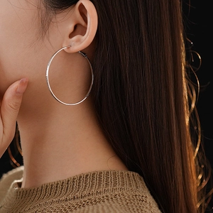 Close-up of large silver round hoop earrings with metallic finish on model's ear
