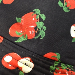 Detail of red apple print on black twill fabric with precision stitching on sun hat