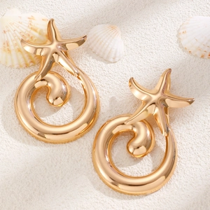 Detail of golden starfish spiral earrings on white sand with sea shells decoration