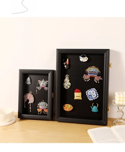 Detail view of two black magnetic shadow boxes for badges and jewelry on a wooden desk