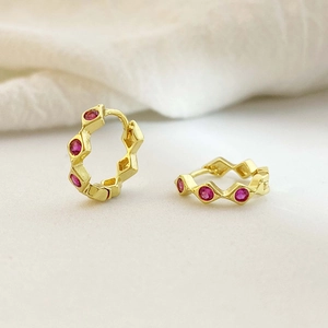 Macro shot of gold-plated wavy hoop earrings with inlaid red gemstones detail