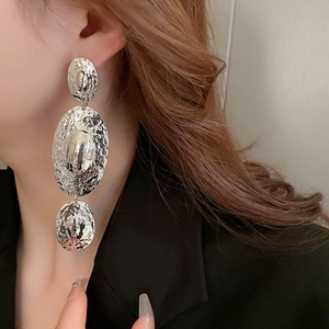 Macro detail of long silver metal drop earrings with irregular hammered texture on a model