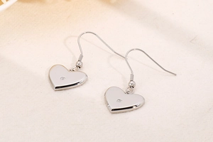 Macro shot of silver heart drop earrings with tiny zircon on beige linen background