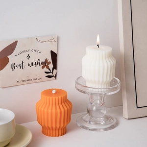 Artistic striped white and orange pillar candles set on clear glass holders in cozy scene