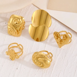 Detail of diverse gold stainless steel rings featuring floral and heart motifs on white stone