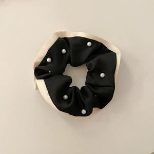 Detalle de coletero de seda negra con borde crema y elegantes adornos de perlas de imitación