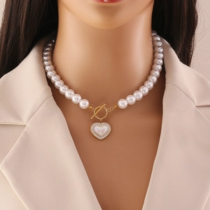 Élégant collier de perles avec pendentif cœur doré et fermoir en T porté par un mannequin