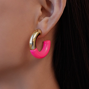 Detailed close-up of a stylish gold and pink acrylic C-shaped hoop earring on a model