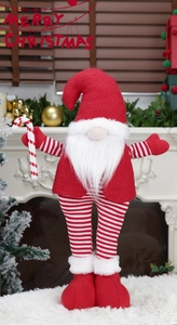 Detail of Christmas gnome with knitted red hat and candy cane by a white fireplace