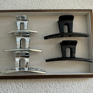 Flat lay of minimalist large silver and matte black shark hair clips in a tray