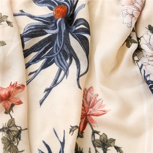 Detailed close-up of beige linen silk scarf fabric with elegant floral print and soft drapes