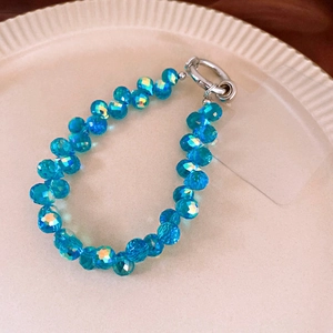 Detailed view of faceted blue crystal phone strap with silver clasp on a textured plate